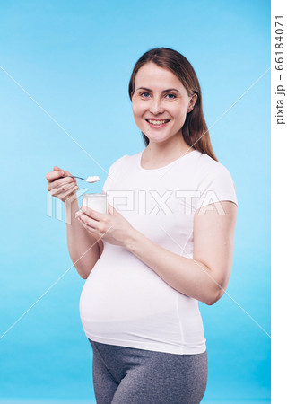 Pretty pregnant woman in activewear holding small plastic jar with bio yoghurt 66184071