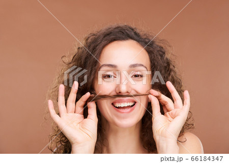 Joyful woman with toothy smile holding bunch of hair between her mouth and nose 66184347