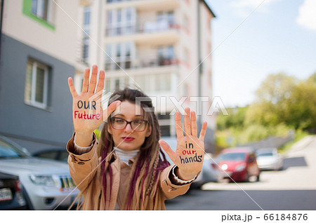 Modern girl with long dreadlocks and eyeglasses in nude color trench is showing hands with written slogan 'Our future in our hands' on some building background. Real estate concept Modern girl with long dreadlocks and eyeglasses in nude color trench is showing hands with written slogan 'Our future in our hands' on some building background. Real estate concept 66184876
