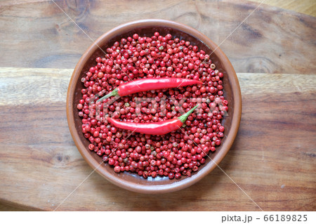 Pink peppercorns and red hot chili peppers in a clay plate standing on a wooden background. 66189825