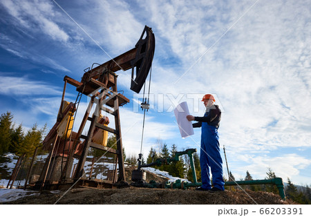 Oil worker standing by oil well pump jack. 66203391