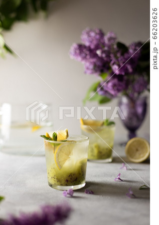 Fresh summer lemonnad with mint and kiwi stands on the table. Nearby is a bouquet of lilacs in a purple vase. Fresh summer lemonnad with mint and kiwi stands on the table. Nearby is a bouquet of lilacs in a purple vase. 66203626