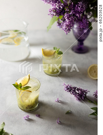 Fresh summer lemonnad with mint and kiwi stands on the table. Nearby is a bouquet of lilacs in a purple vase. 66203628
