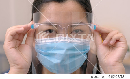 Portrait of an Asia young female who is wearing a face shield with mask rounded around her face from a frontal perspective to protect her glasses and eyes prepare to new normal. Coronavirus pandemic. 66208584