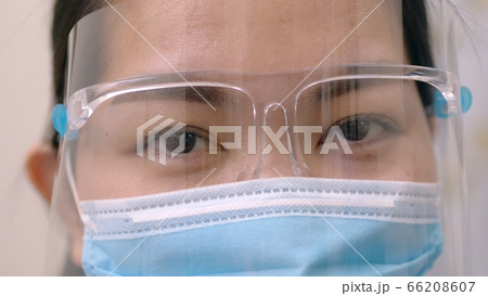 Portrait of an Asia young female who is wearing a face shield with mask rounded around her face from a frontal perspective to protect her glasses and eyes prepare to new normal. Coronavirus pandemic. Portrait of an Asia young female who is wearing a face shield with mask rounded around her face from a frontal perspective to protect her glasses and eyes prepare to new normal. Coronavirus pandemic. 66208607