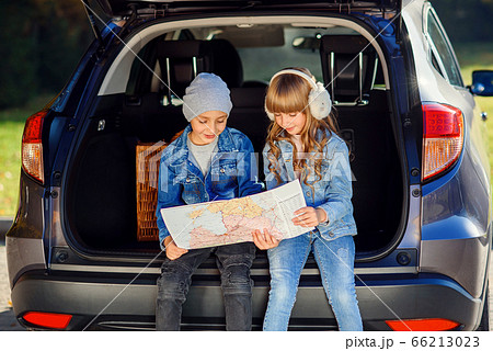 Agreeable boy and girl are looking at the road map while sitting in the auto's trunk and discussing the move direction. Family vacation trip by car. 66213023