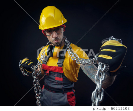 a man in a construction repairman's overalls holds a metal chain in his hands 66213108