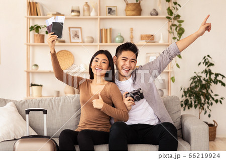 Couple Holding Tickets And Passports Gesturing Thumbs-Up Sitting On Couch 66219924