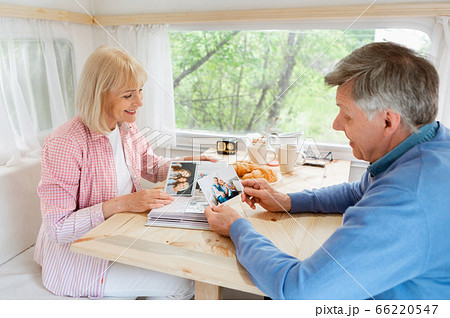 Senior married couple looking through family album with photos inside of camping vehicle 66220547