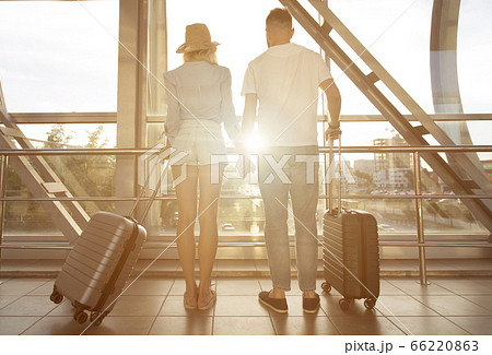 Rear view of couple standing in airport with luggage Rear view of couple standing in airport with luggage 66220863