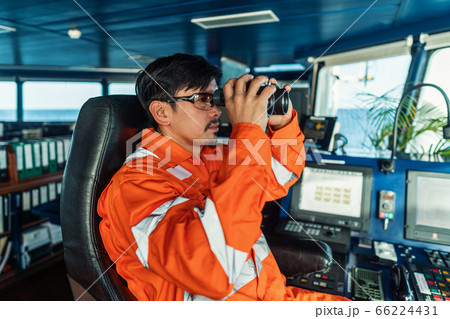 Filipino deck Officer on bridge of vessel or ship looking through binoculars 66224431