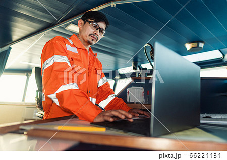 Filipino deck Officer on bridge of vessel or ship. He is using laptop, electronic paperwork at sea 66224434