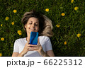 top view of young blonde woman lying on grass and using smartphone 66225312