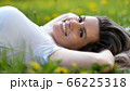 Woman lies on green grass, relaxing outdoors looking happy and smiling 66225318