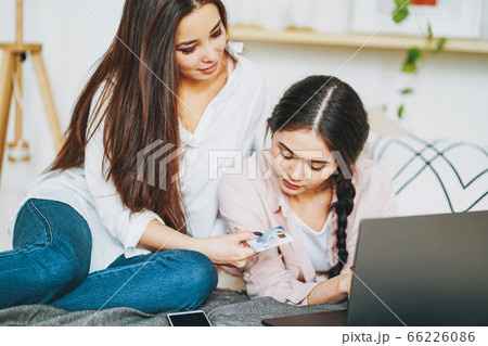 Young carefree brunette girls friends buy online by credit card on the laptop Young carefree brunette girls friends buy online by credit card on the laptop 66226086