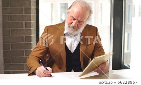Handsome old businessman in classic suit sits at Desk in his office 66228967