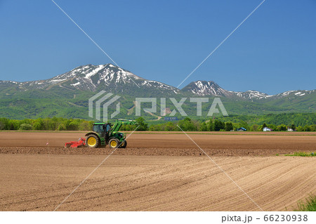 初夏の北海道倶知安町で残雪のニセコ連峰と畑を耕している風景を撮影の写真素材