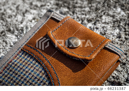 Rivet of handmade wallet of brown leather and checkered textile on stone background. Men's accessory. Rivet of handmade wallet of brown leather and checkered textile on stone background. Men's accessory. 66231387