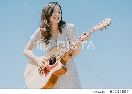 Beautiful woman playing guitar on blue sky background Beautiful woman playing guitar on blue sky background 66235897