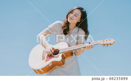 Beautiful woman playing guitar on blue sky background Beautiful woman playing guitar on blue sky background 66235899