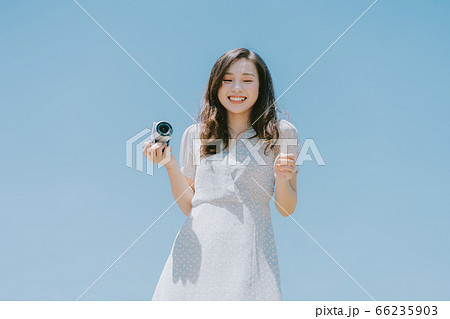Beautiful woman holding a camera on blue sky background Beautiful woman holding a camera on blue sky background 66235903