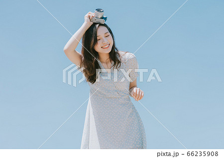 Beautiful woman holding a camera on blue sky background Beautiful woman holding a camera on blue sky background 66235908