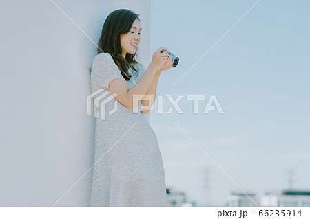 A beautiful woman lean on the wall and holding a camera 66235914