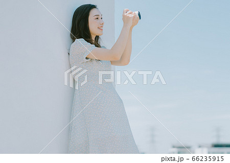 A beautiful woman lean on the wall and holding a camera 66235915
