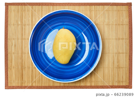 pale yellow mango on a blue plate on a cane place 66239089