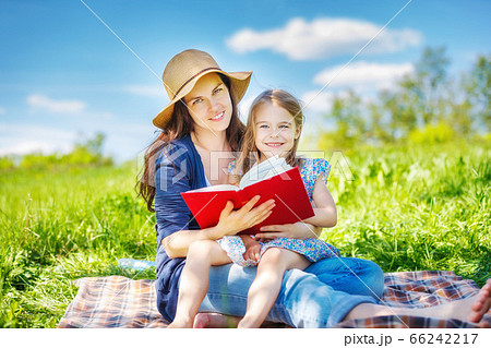 Mother and daughter reading book on green summer meadow 66242217