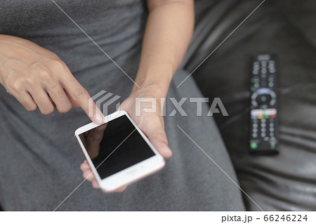 The hand is pressing the phone and remote control to select the channel by application in phone.Spend leisure time at home watching a movie. The hand is pressing the phone and remote control to select the channel by application in phone.Spend leisure time at home watching a movie. 66246224