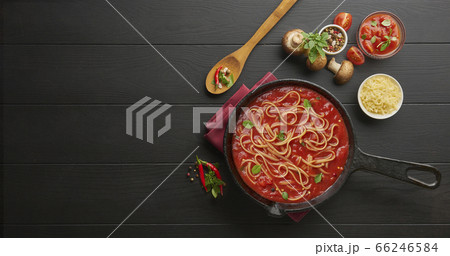 Homemade boiling italian pasta with tomato sauce in cast iron pan served with red chili pepper, fresh basil, cherry-tomatoes and spices over black rustic wooden background, cooking food concept 66246584