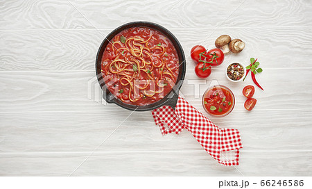 Cooking spaghetti with boiled tomato sauce in cast iron pan served with chili pepper, fresh basil, cherry-tomatoes and spices over white texture wooden background, ingredients food concept Cooking spaghetti with boiled tomato sauce in cast iron pan served with chili pepper, fresh basil, cherry-tomatoes and spices over white texture wooden background, ingredients food concept 66246586