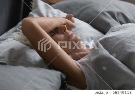 Exhausted mature woman sleeping peacefully in home bed 66249118