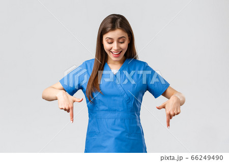 Healthcare workers, prevent virus, covid-19 test screening, medicine concept. Happy and excited pretty female nurse or doctor in blue scrubs, smiling as reading great news, pointing fingers down 66249490