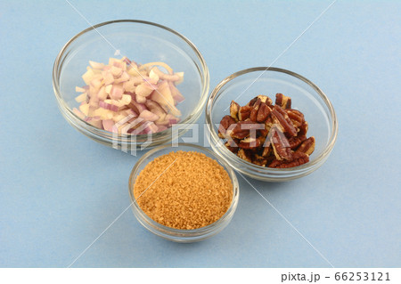Ingredients of chopped shallot onion, brown sugar and pecan nuts in glass bowls for cooking on blue background 66253121