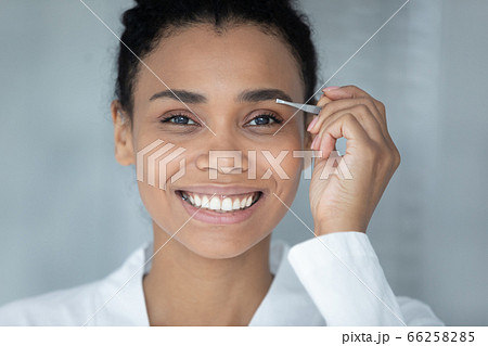 Head shot smiling African American woman plucking eyebrows with tweezers 66258285
