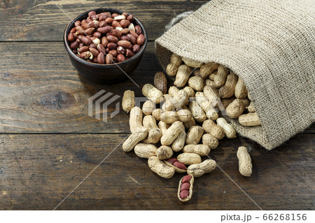 Inshell peanuts in burlap, on brown wooden background. next is a plate with peanuts. Inshell peanuts in burlap, on brown wooden background. next is a plate with peanuts. 66268156