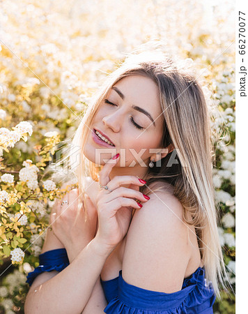 Sensual calm portrait of beautiful hipster woman in blooming bush with white flowers of spirea. Copy space. Stylish blonde woman in blue dress in garden 66270077