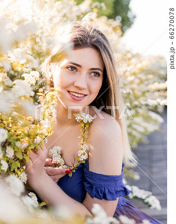 Sensual calm portrait of beautiful hipster woman in blooming bush with white flowers of spirea. Copy space. Stylish blonde woman in blue dress in garden 66270078