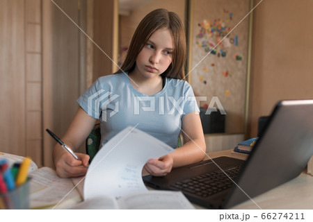 Teenager girl writing in notebooks and assignment notes, home education, preparation for college and school. Video conference on the Internet. Online communication with a teacher in a laptop. Teenager girl writing in notebooks and assignment notes, home education, preparation for college and school. Video conference on the Internet. Online communication with a teacher in a laptop. 66274211