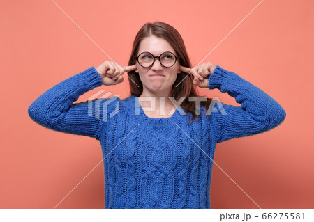Young female in glasses having discontent look plugging her ears being annoyed with noise 66275581