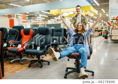 Couple rides on office chair in furniture store Couple rides on office chair in furniture store 66276686