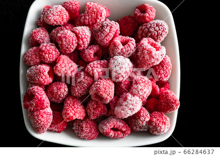 frozen ripe raspberries in a white deep plate on a black background 66284637