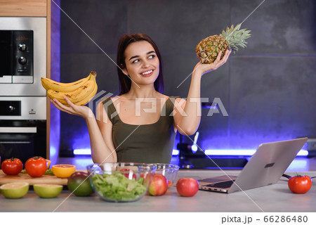 Woman choosing between dessert and fruits at table in kitchen. Healthy diet Woman choosing between dessert and fruits at table in kitchen. Healthy diet 66286480