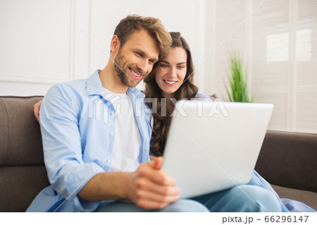 Young couple in denim sitting on a sofa watching something online and smiling 66296147