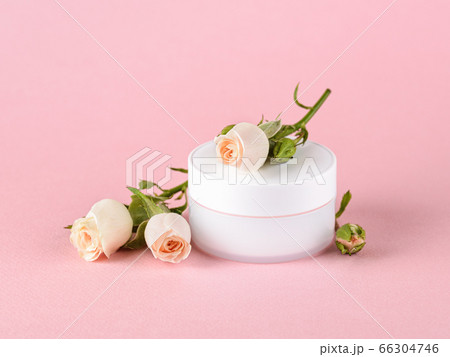 Facial cream and small roses of light peach color on a pastel pink background. Facial cream and small roses of light peach color on a pastel pink background. 66304746