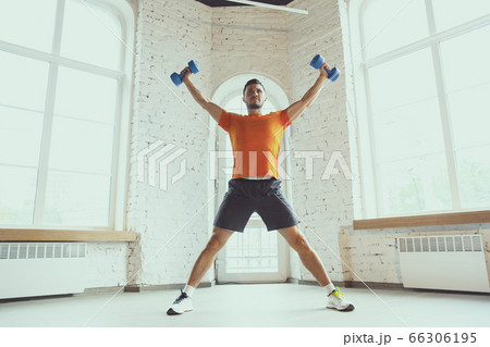 Young caucasian man training at home during quarantine of coronavirus outbreak, doing exercises of fitness, aerobic. Staying sportive during insulation. Young caucasian man training at home during quarantine of coronavirus outbreak, doing exercises of fitness, aerobic. Staying sportive during insulation. 66306195