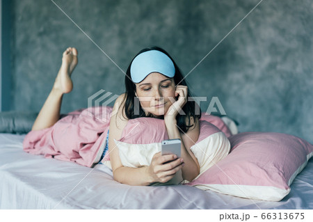 .the girl in bed woke up and looks at the phone .the girl in bed woke up and looks at the phone 66313675