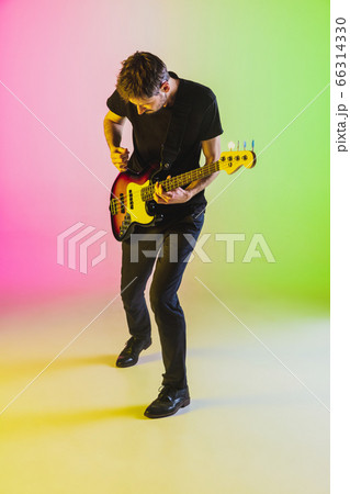 Young caucasian musician playing bass guitar in neon light on pink-green background Young caucasian musician playing bass guitar in neon light on pink-green background 66314330